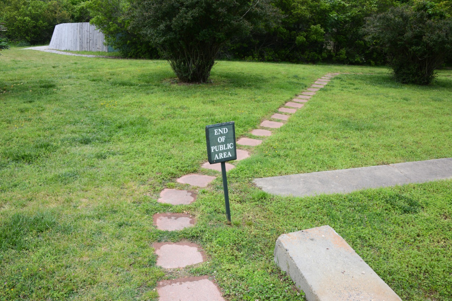A sidewalk leading down a grassy area with a sign that says, "End of Public Area."
