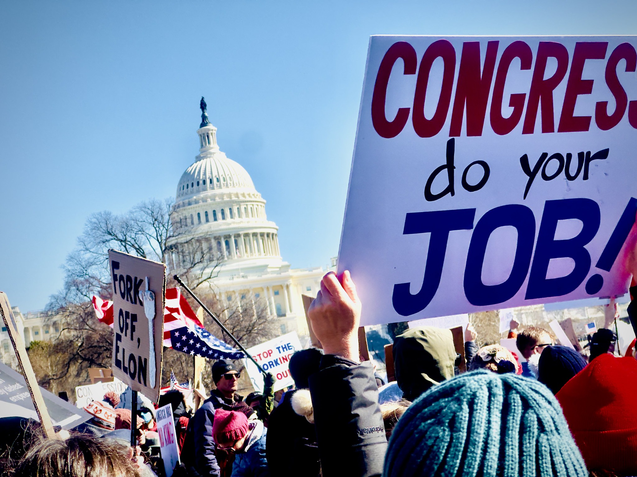 Protesters rallying in front of the white house. One person holds a poster that reads, "Congress, do your job!"