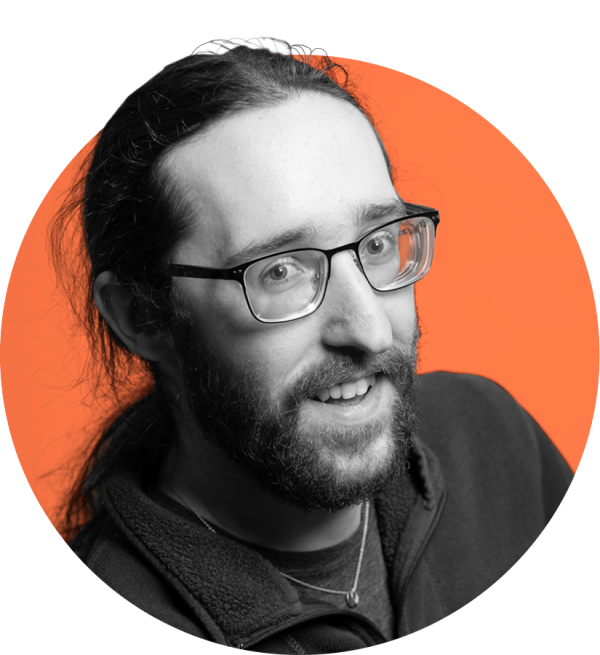 A long-haired caucasian man with glasses and a beard, smiling 