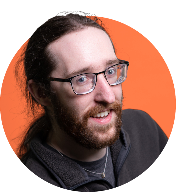 A long-haired caucasian man with glasses and a beard, smiling 