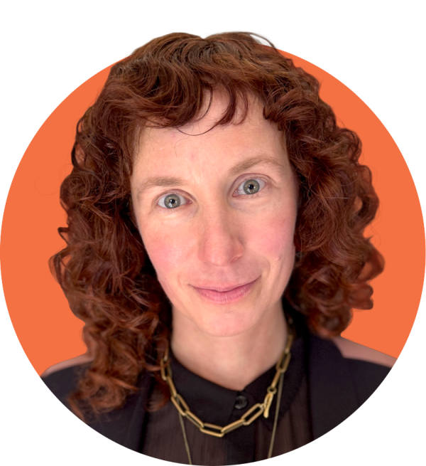 A white nonbinary femme person with curly red hair looking into the camera with a slight smile