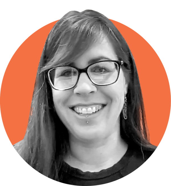 A white woman with curly straight brown hair wearing glasses looking into the camera with a smile.