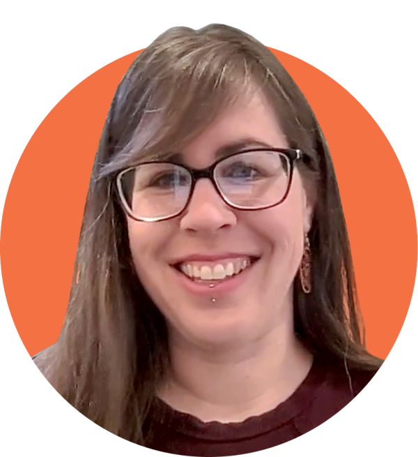 A white woman with curly straight brown hair wearing glasses looking into the camera with a smile.